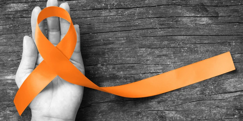 Orange ribbon in hand on wooden background.