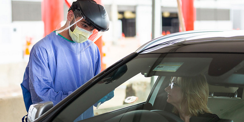 Healthcare worker in PPE interacting with driver.