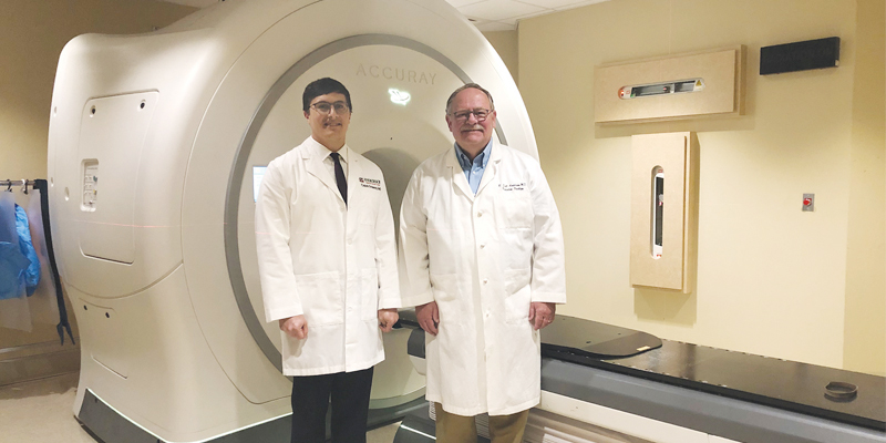 Two doctors standing by medical radiation therapy machine.