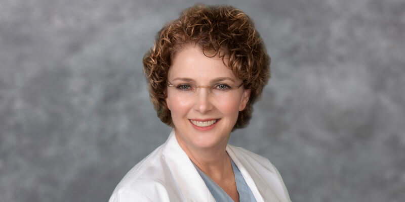 Smiling woman with short hair, wearing glasses and lab coat.