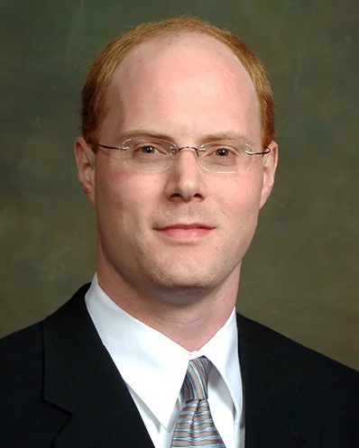 Bald man with glasses in formal black suit and tie.