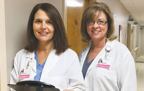 Two nurses smiling in hospital corridor.