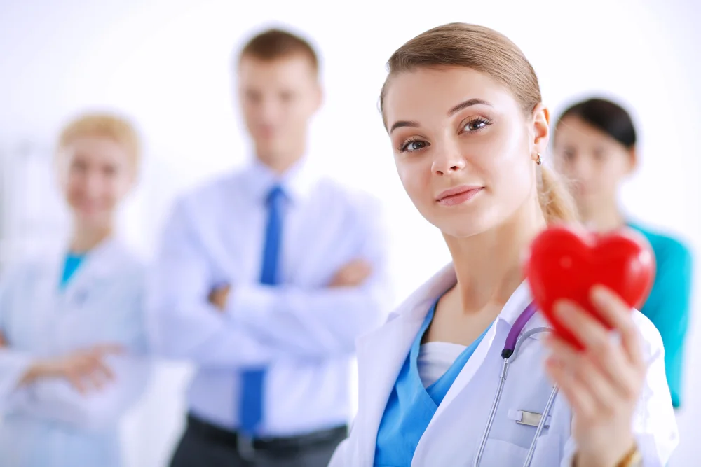 Female doctor holding red heart with colleagues behind