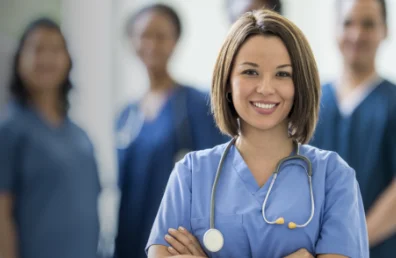 Smiling nurse with stethoscope, team in background.