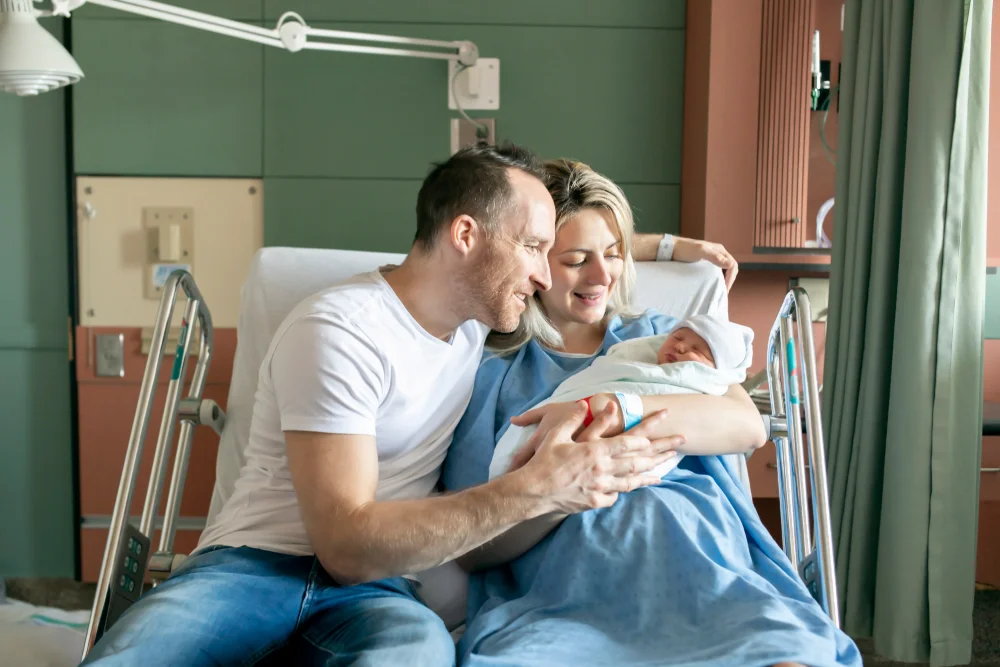 New parents cradling newborn in hospital room.