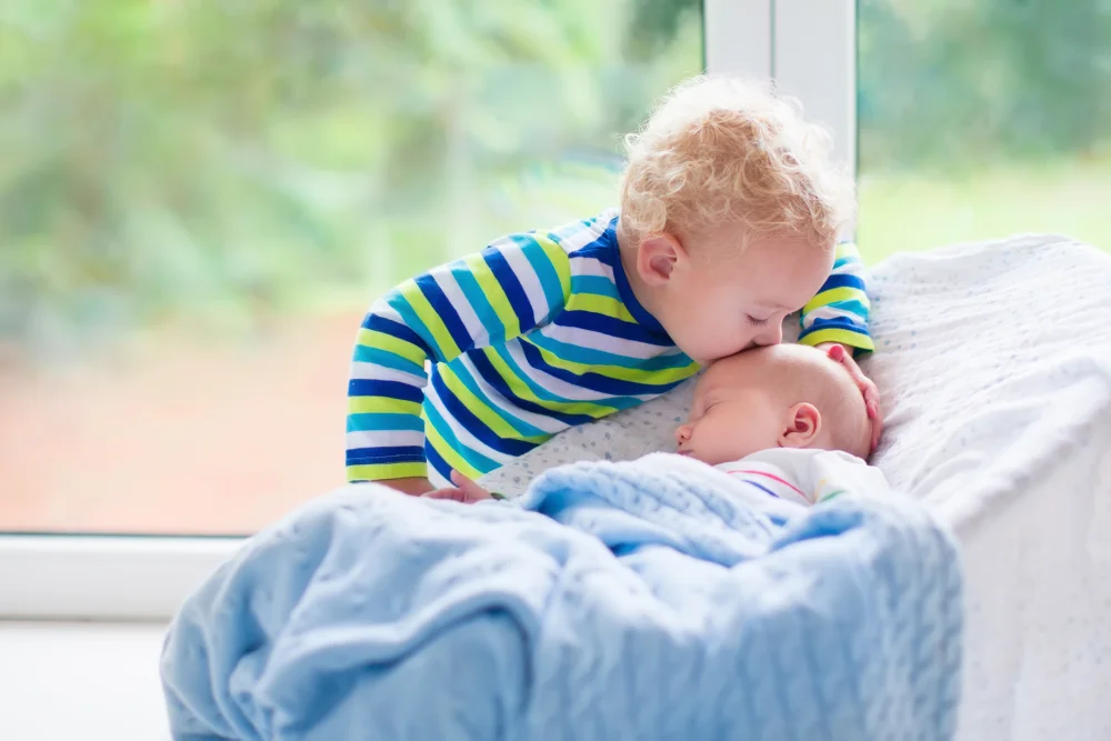 Toddler kissing sleeping newborn, family bonding moment.